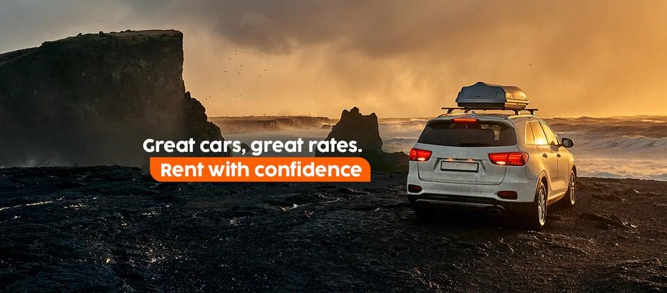 White SUV with rooftop cargo box parked on a rugged coastal road at sunset — great cars, great rates, rent with confidence